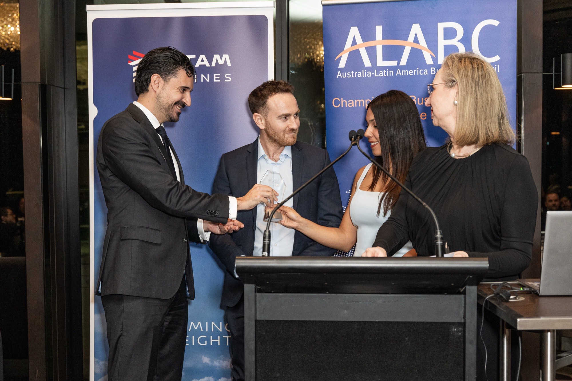 The Warriors representatives receiving the ALABC Business Excellence Award at the lectern, with the LATAM Airlines and ALABC banners behind them